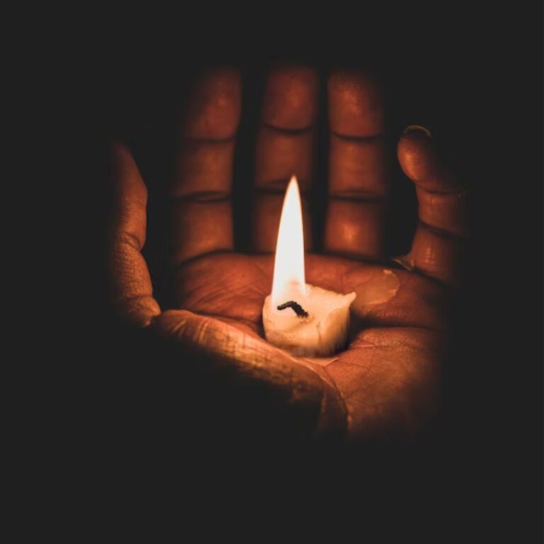 a stub of a candle in a palm illuminating the palm in the dark